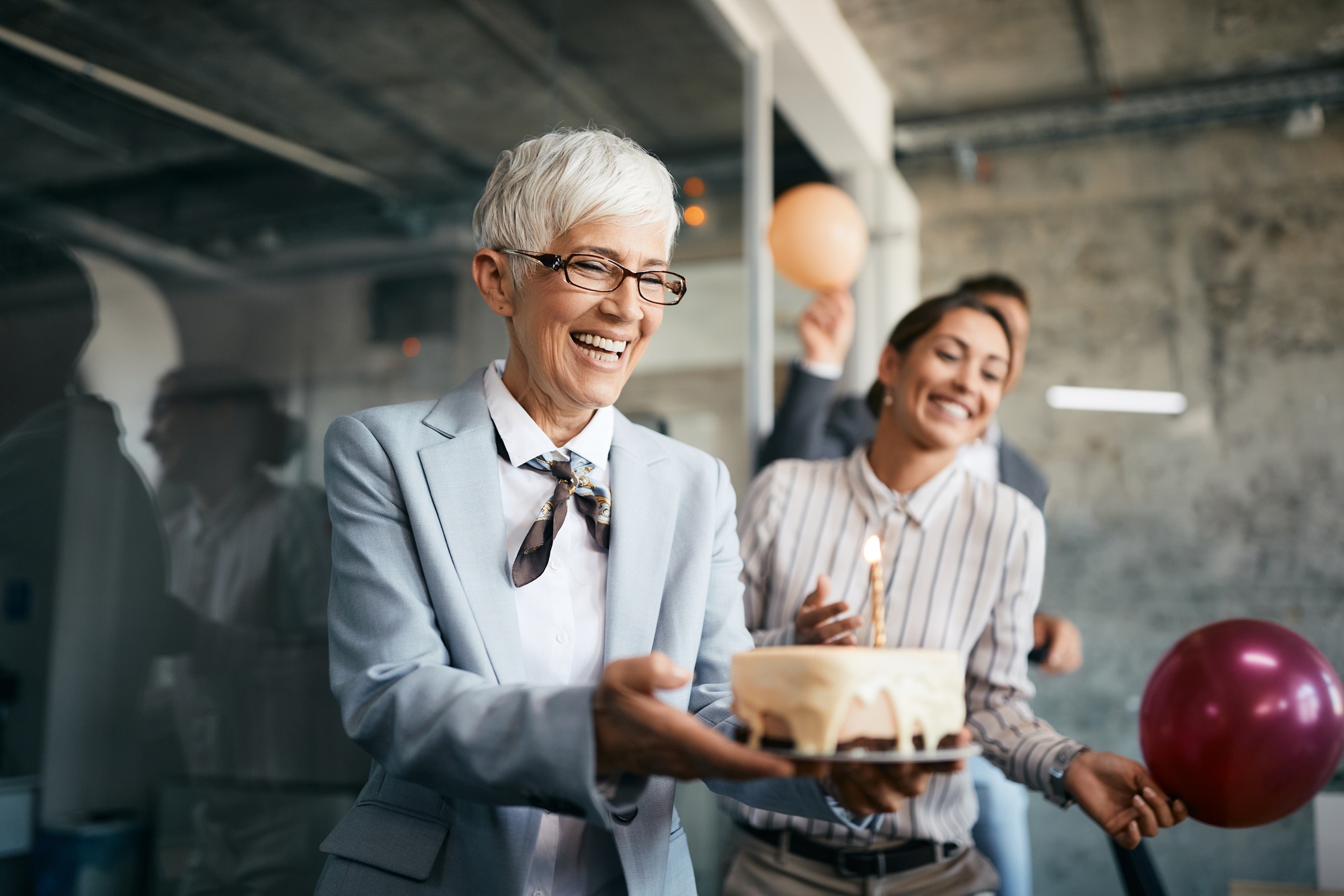 Happy senior businesswoman carrying Birthday cake on surprise party in the office.